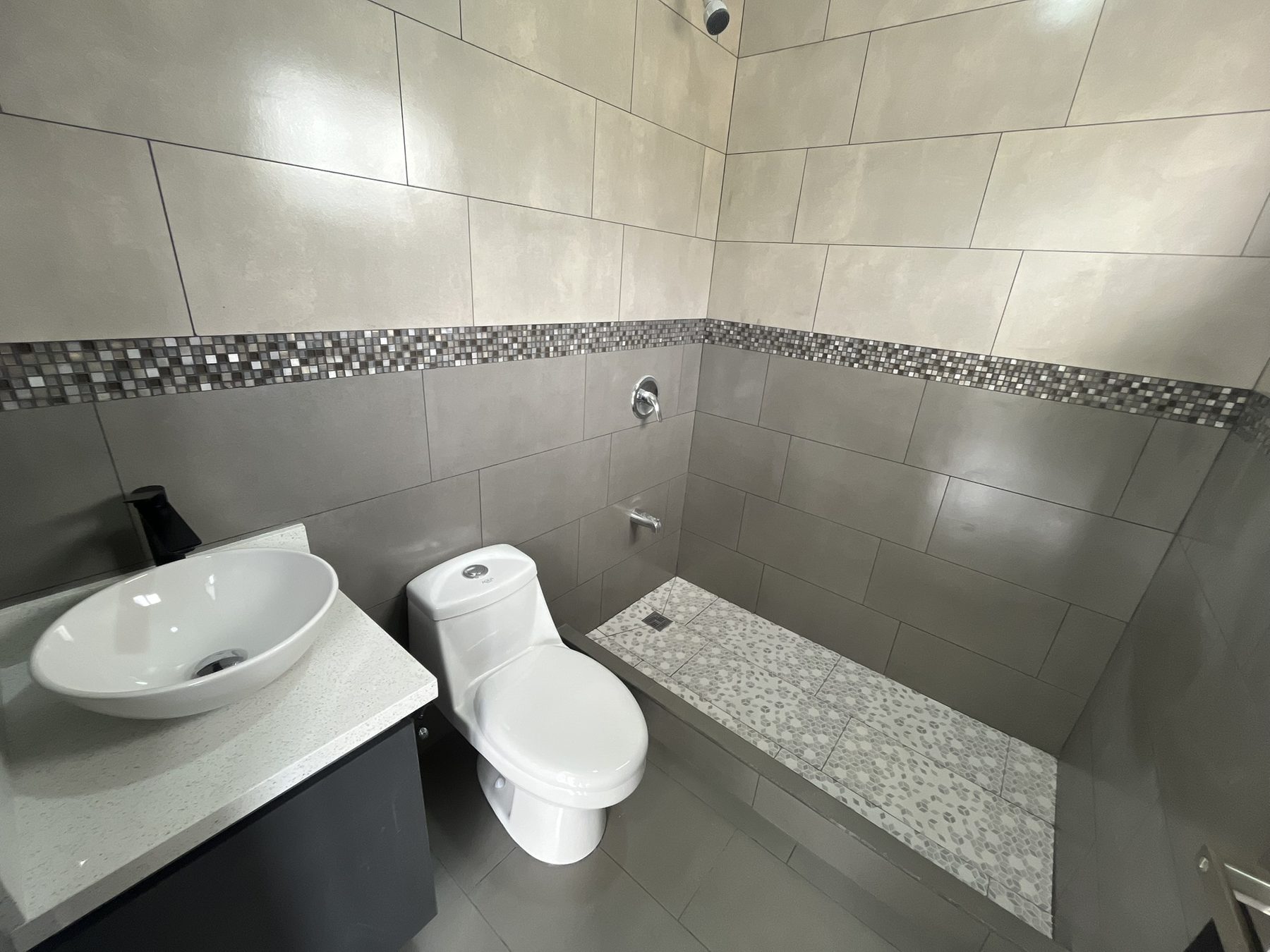 Baño completo con mosaico decorativo, lavatorio de sobreponer y ducha