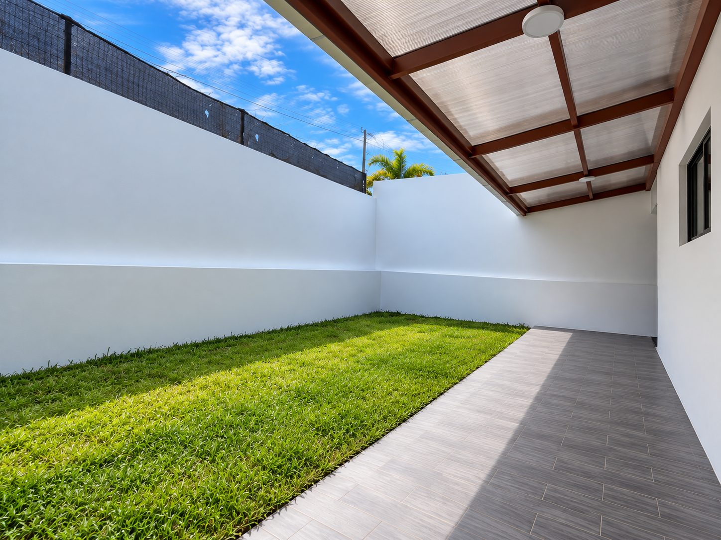 Patio trasero con zacate, terraza enchapada y techo de policarbonato