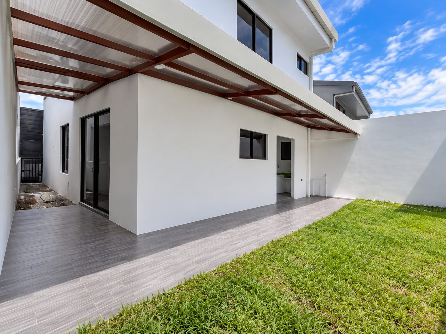 Fachada trasera de la casa con terraza techada y zacate