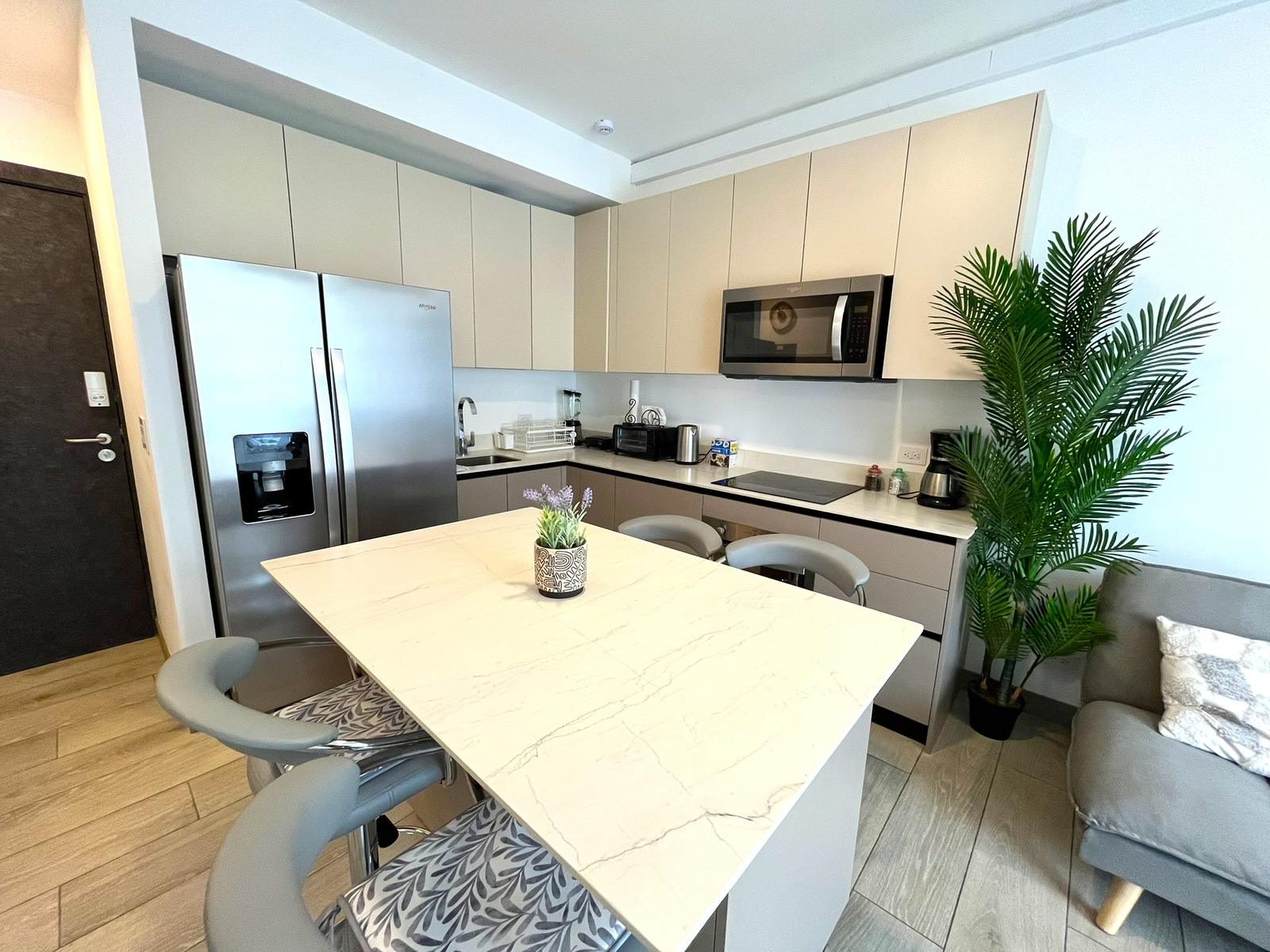 Cocina en L con refrigeradora de dos puertas, microondas y isla de cuarzo