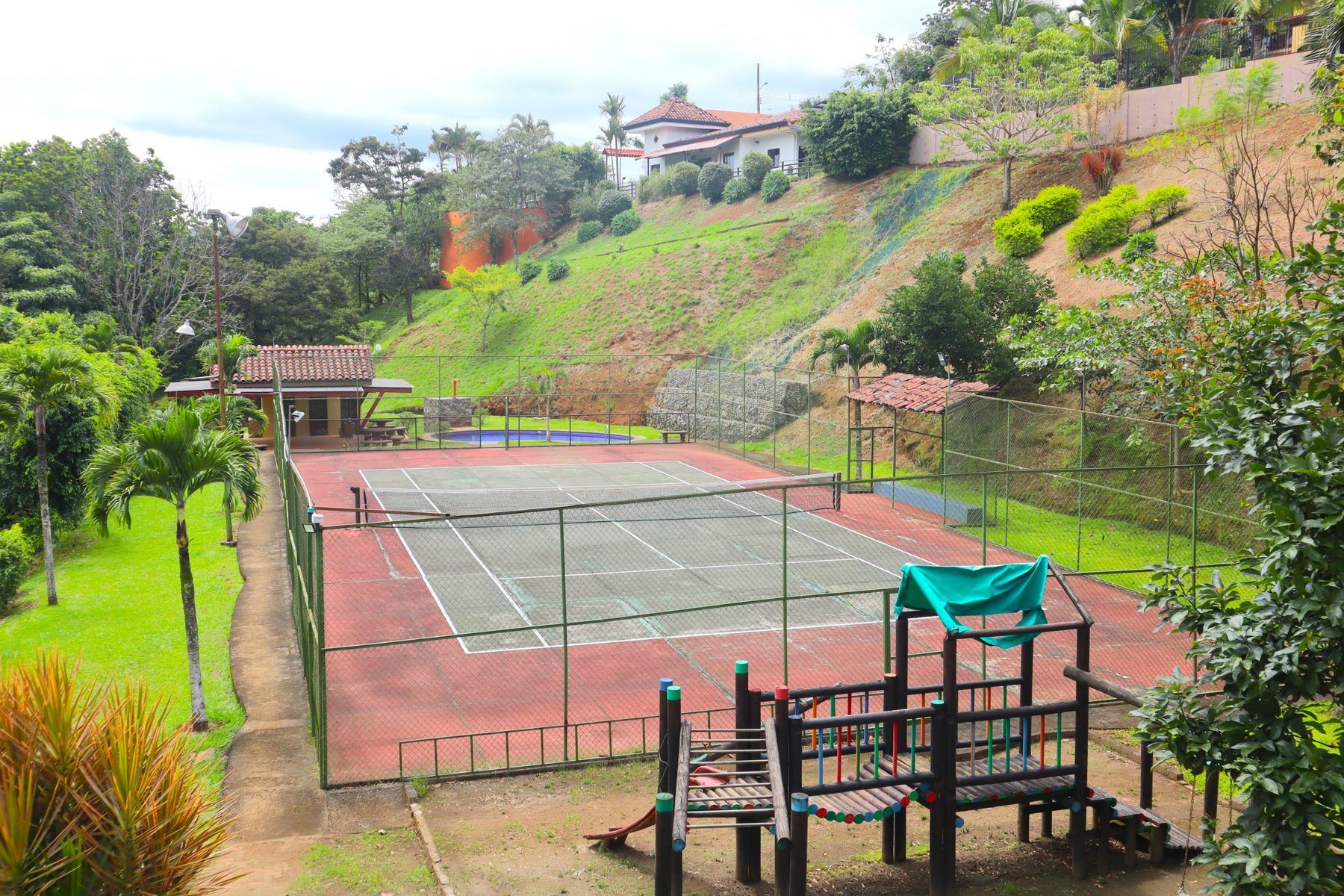 Cancha de tenis del Condominio Loma Verde con la piscina y el rancho al fondo